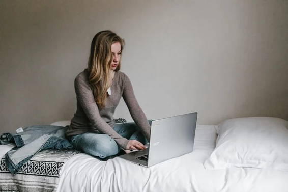 mujer sentada en una cama con una computadora gris y escribiendo