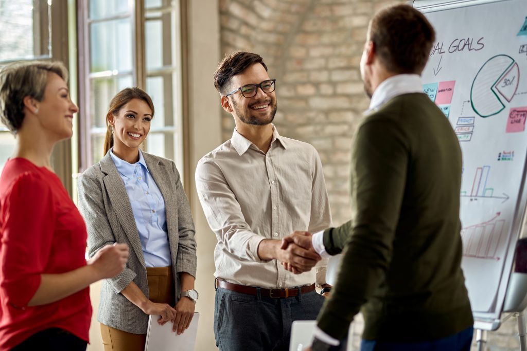 Compañeros de trabajo felices dándose la mano después de la presentación de negocios en la oficina